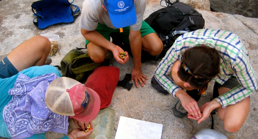 Three people sit on a rocky surface and examine a piece of paper between them.